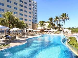 a swimming pool with chairs and umbrellas at a resort at Mercure Salvador Rio Vermelho in Salvador