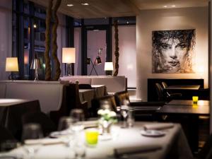 ein Restaurant mit Tischen und Stühlen und einem Gemälde einer Frau in der Unterkunft Pullman Eindhoven Cocagne in Eindhoven