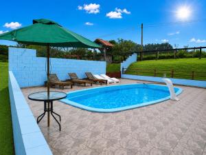 a pool with an umbrella and chairs and a table at Sítio Santo Expedito in Salesópolis