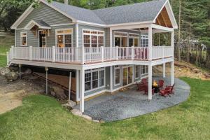 a large house with a deck and chairs in the yard at Elegant lakefront home near Bar Harbor & Acadia with modern kitchen, lake views in Orland