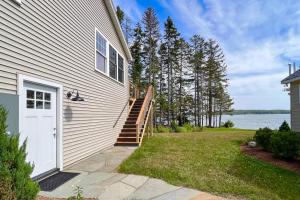 a house with a white door and stairs next to the water at Newly-built waterfront home with fast WiFi, furnished deck, & washer/dryer in Waldoboro