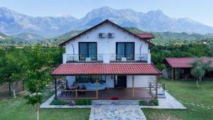 a white house with a deck and mountains in the background at Guesthouse Micaj LUNI in Himare