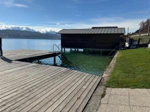 a wooden dock with a building on the water at Lakeside Central Apartment Wörthersee - Free covered Parking, Train & Bus & Supermarket with Supercharger in Sekull