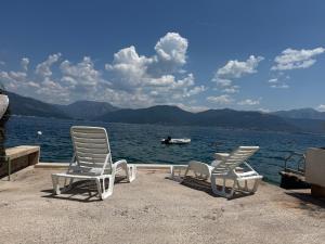 two lawn chairs and a boat in the water at Zo-Mi Apartments in Tivat