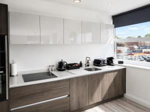 a kitchen with white cabinets and a sink and a window at Luxury Central Solihull Apt - King Bed, Sofa Bed & 2 Parking Spaces in Solihull +6 photos