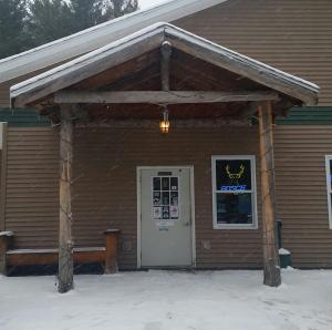 a building with a porch and a door in the snow at Deer Valley Trails in Saint Regis Falls