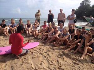 a group of people sitting in the sand on the beach at Moon Garden Hotel And Restaurant in Arugam Bay