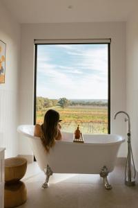a woman sitting in a bath tub in a bathroom with a large window at Monapilla Escape in McLaren Vale