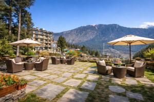 a patio with chairs and umbrellas with mountains in the background at LN Grand Premium & Luxury Suites, Manali in Manāli