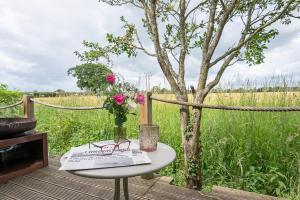a table with a vase of flowers and a book at Toad Hall Lodges - Luxury Glamping Lodges Near Southwold! in Wangford