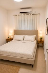 a bedroom with a large white bed with two tables at סוויטת אריאל - סוויטה משפחתית עם מרפסת בבית שאן in Bet Sheʼan