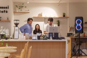 three people standing around a counter with a laptop at Bonsai Cafe and Stay - B&B Dormitory in Tokyo