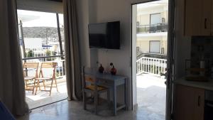 a living room with a television and a table and a balcony at Veranda Agia Marina in Agia Marina Aegina
