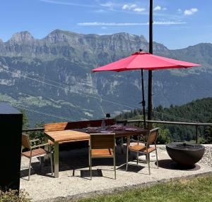 a table and chairs with a red umbrella and mountains at Chalet Waldhüsli - CharmingStay in Quarten