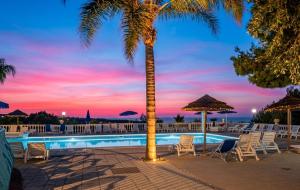 a palm tree next to a swimming pool with a sunset at RESIDENCE EMARINE con SERVIZIO SPIAGGIA INCLUSO in Peschici