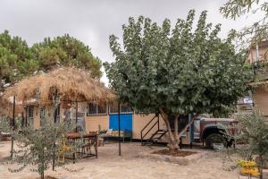 a house with a tree and a table and a truck at Maison Jwar - Charming Caravan Experience - Unique Summer Getaway in Jiwār al Ḩawz