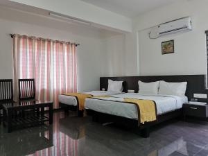 a bedroom with two beds and a table and a chair at Hotel Gateway Inn in Kushālnagar