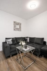 a living room with a black couch and a glass table at ALURE RESIDENCES 1 & 24h self check-in, free parking in front of the apartment building, new building, terrace, cafe with breakfast in the apartment building, next to the aqua park in Banská Bystrica
