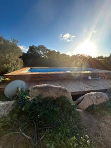 a wooden deck with a swimming pool with the sun shining at Chalet Valle di Corti in Pianottoli-Caldarello +20 photos