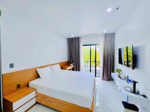 a bedroom with a large white bed and a television at Bay Homestay in Cam Lâm