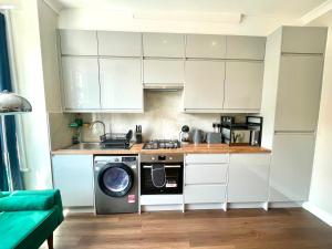a kitchen with white cabinets and a washing machine at Stylish 2BR Flat 3 Mins to Wembley Stadium in London