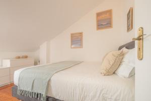 a bedroom with a bed with white sheets and pictures on the wall at Baleal Happiness Surf House in Baleal