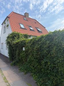 a white house with a red roof and a hedge at 24 h chek in big house in Copenhagen