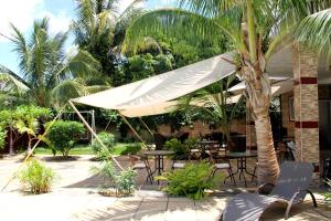 un patio con mesas, sillas y una sombrilla blanca en Lariad BnB, en Flic en Flac