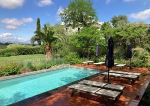 a swimming pool with two benches and an umbrella at Clos Des Aspres in Ortaffa