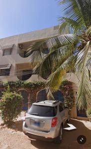 a car parked in front of a building with a palm tree at Guest House MM in Saly Portudal