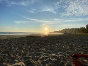 a person sitting on a beach with the sun setting at HIDDEN HOSTAL MONTANITa in Montañita