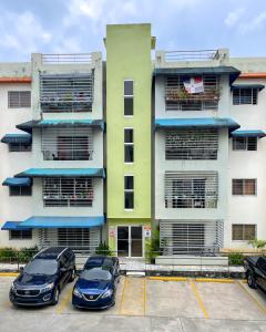 two cars parked in a parking lot in front of a building at 3 dormitorios y confortable apartamento in Santo Domingo