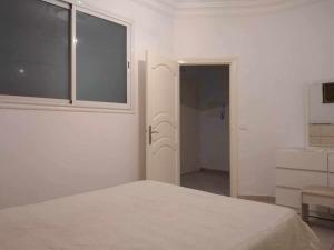 a white bedroom with a bed and a window at Appartement Ezzdine sfaxi in Kelibia
