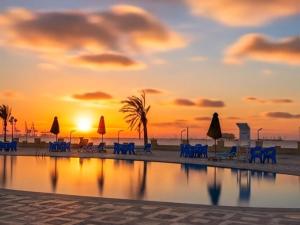 a sunset on the beach with chairs and umbrellas at Amwaj Hotel in Alexandria