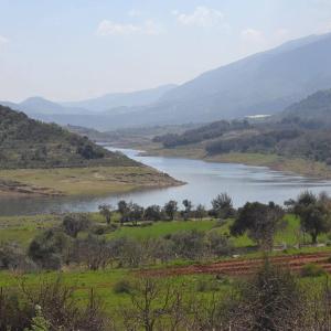 a lake in the middle of a field with mountains in the background at Saghbine bungalows in ‘Ayn Zubdah