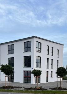 a white building with two trees in front of it at Modernes Studio mit Küche, WLAN, Parkplatz in Dingolfing