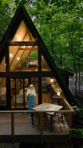 a woman standing on the deck of a cabin at Wilewood A-Frame, Romantic Treehouse Getaway, Hot Tub in Abbeville