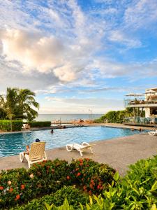 a person sitting in a chair next to a swimming pool at Resort Playa Azul Departamentos Frente al Mar in Tonsupa