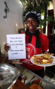 a woman holding a sign and a plate of pizza at butterfly lodge in Brufut