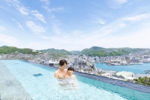 a man and a child in a swimming pool with a city at Ooedo Onsen Monogatari Premium Nagasaki Hotel Seifu in Nagasaki