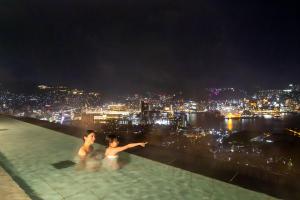 two people in a infinity pool with a city at night at Ooedo Onsen Monogatari Premium Nagasaki Hotel Seifu in Nagasaki