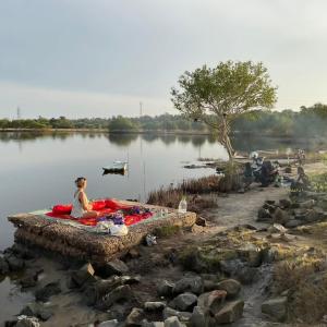 a woman sitting on a blanket next to a lake at Nimal's white house in Nilaveli