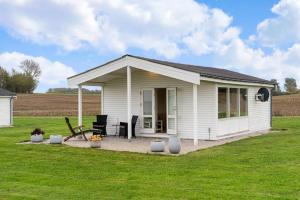 a small white house with a patio in a field at Sct Knudsborg - 12J - Summerhouse on the beach in Brenderup