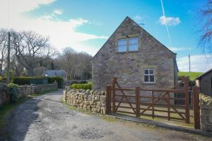 a stone house with a wooden gate and a fence at The Old Stables in Bamburgh