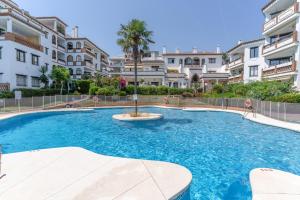 a swimming pool with a palm tree in front of some buildings at Sunny Calahonda Park in Sitio de Calahonda