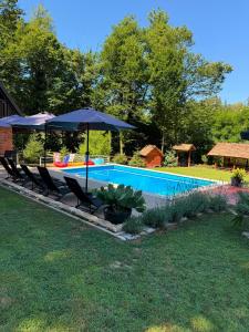 a pool with chairs and umbrellas in a yard at Dunja Cabin - Forest House with Pool in Banja Luka