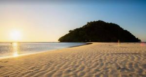 a sandy beach with a island in the water at Kelambu Beach Villa in Kudat