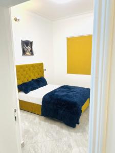 a bedroom with a bed with blue sheets and a yellow headboard at His Goodness - Apt Two! in Kampala
