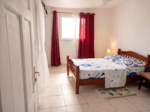 a bedroom with a bed and a window with red curtains at Appartement 3 chambres à Ducos in Ducos