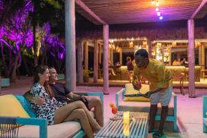 a man standing next to two women sitting on chairs at Furaveri Maldives - COMPLIMENTARY ROUND-TRIP SEAPLANE TRANSFER FOR TWO FOR A MINIMUM OF 5 NIGHTS OR MORE FOR STAYS 1ST MAY 2026 TO 23RD DECEMBER 2026 in Raa Atoll